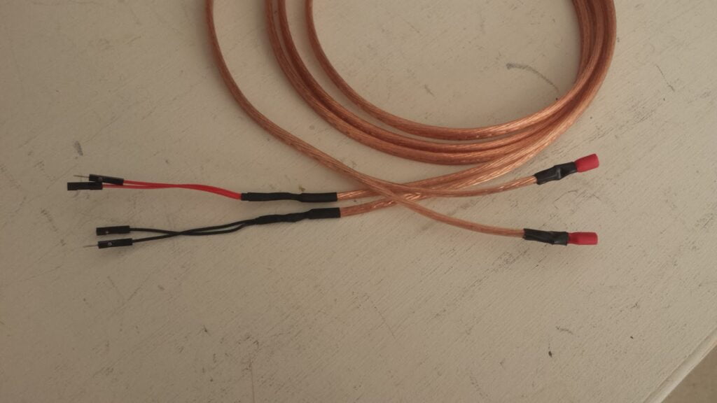 A length of speaker wire. On one end of each of the pair or wires, male & female patch panel wire has been soldered. On the other end of each wire, a terminal connector is soldered in place.