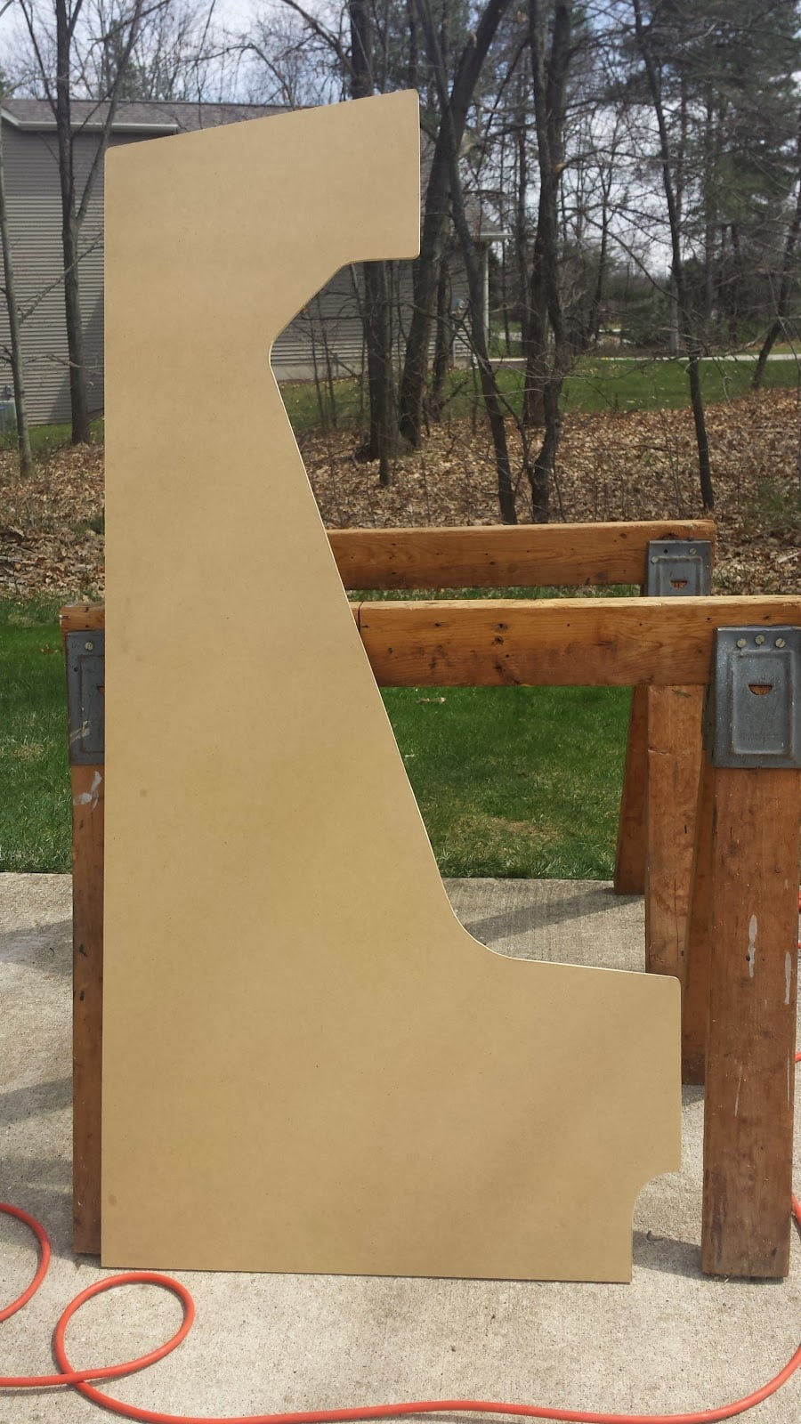 A quarter-inch MDF cutting termplate for the top half of the side on an arcade cabinet.  The template is outdoors, leaned against a sawhorse.