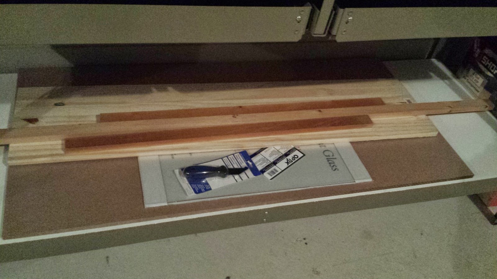 Sheets of MDF and lengths of pine lumber, stacked on the bottom shelf of a toolbench