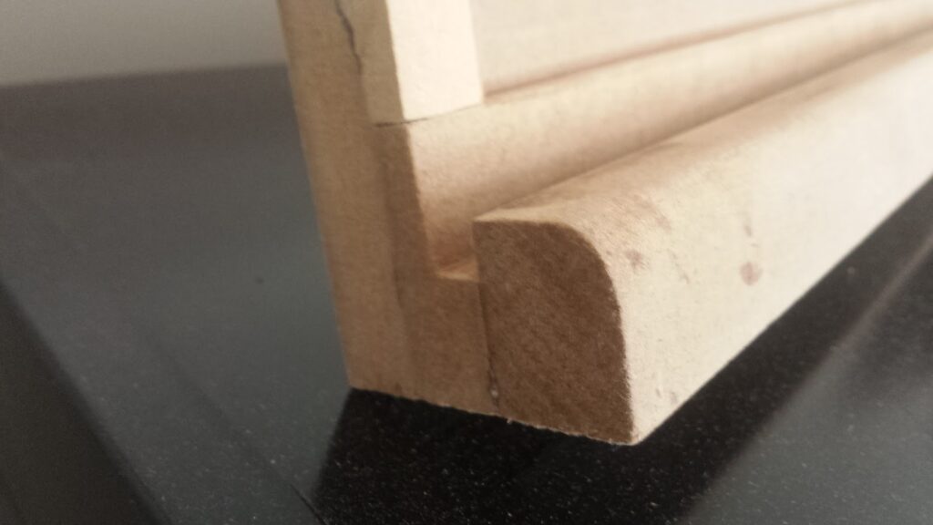 Close-up of bottom edge of screen bezel section. Three layers of MDF are glued together, forming a rounded bezel, and a channel for the protective screen glass to rest inside.