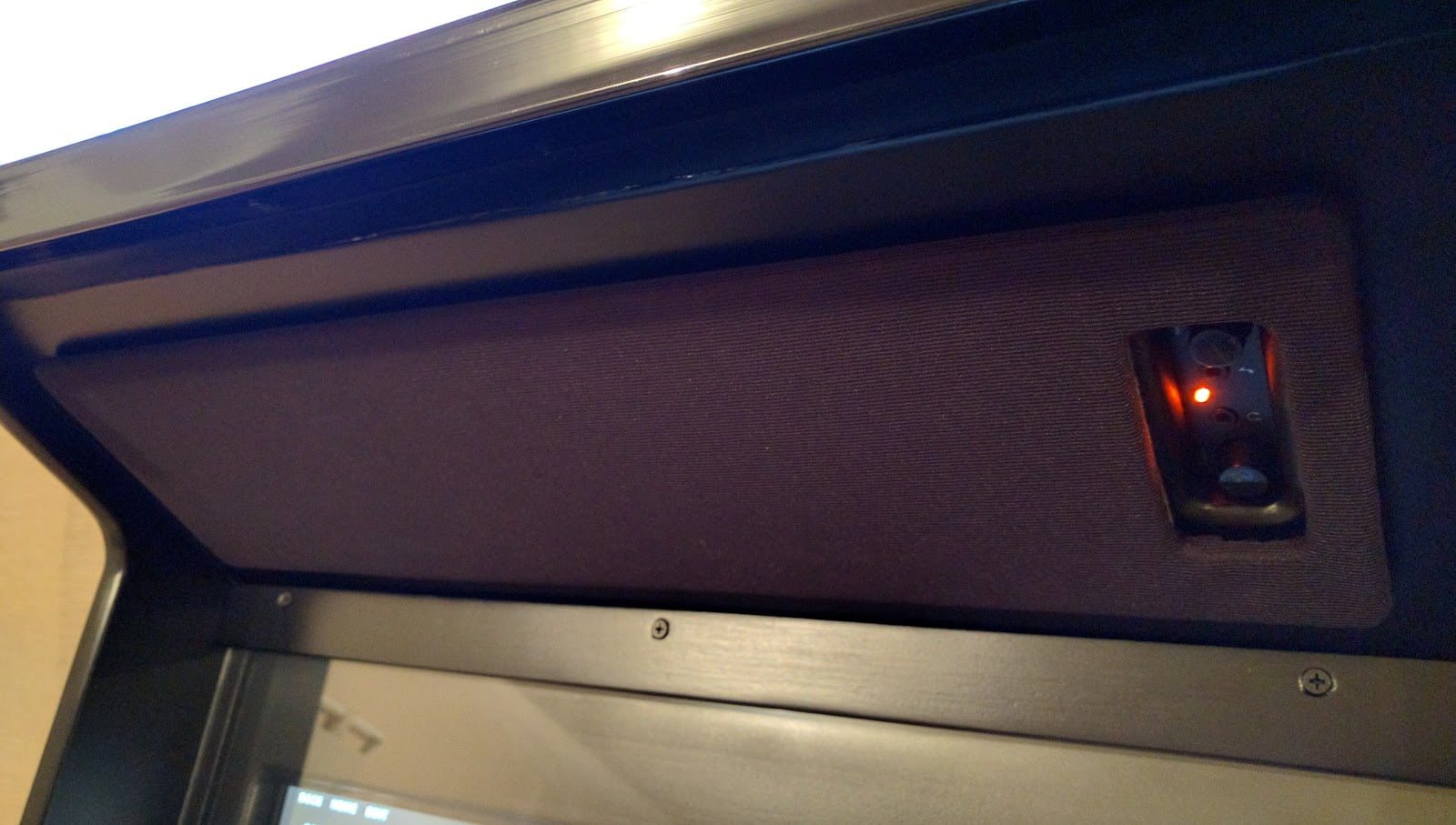 A speaker grill, above the monitor on an arcade cabinet. The grill is a rectangonal panel covered completely in black speaker fabric. On the right side of the panel is a cutout, giving access to the volume & power controls for the speakers mounted behind the panel.