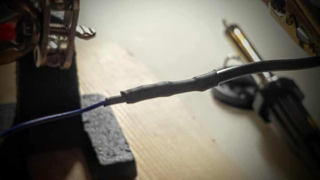 Close up of a thin wire, soldered to a thicker wire.  A small length of heat-shrink tubing is attached to the thinner wire, giving that wire sufficient diameter to make it possible for a second heat-shrink to bridge the solder between both wires.