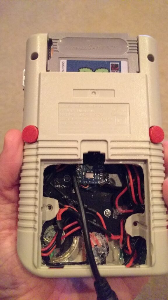 Rear view of Game Boy Zero handheld, with the plastic shell in place.  The battery cover has been partially Dremeled away to give room for a lithium battery and various electronic components.