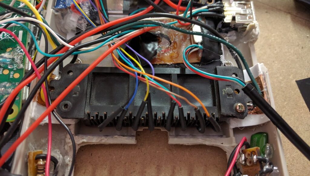 Looking inside a Game Boy Zero homemade handheld.  Multiple wires are attached to various circuit boards and electronic components.