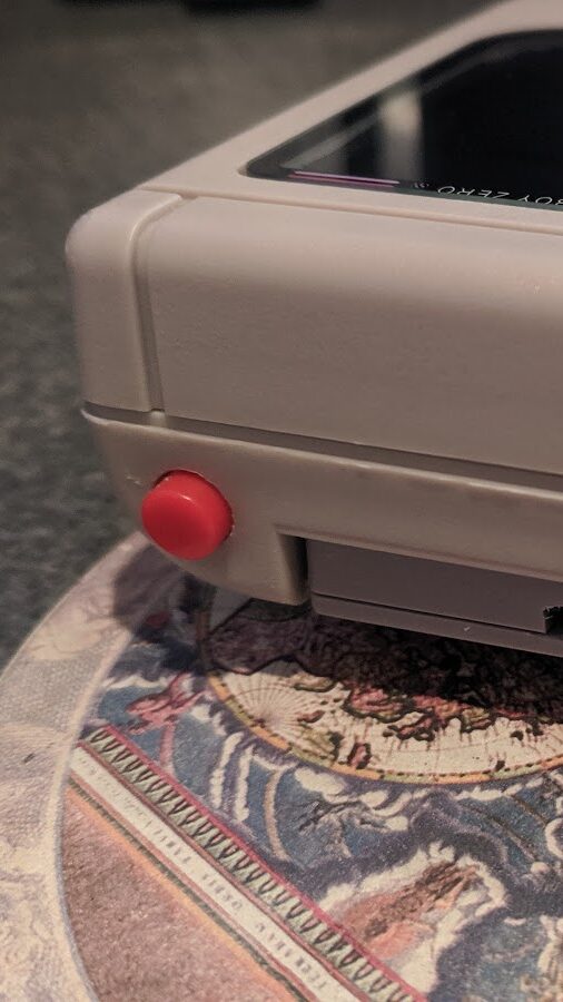 Top view of fully-assembled Game Boy Zero handheld.  A red button has been retrofitted into the top of the shell.