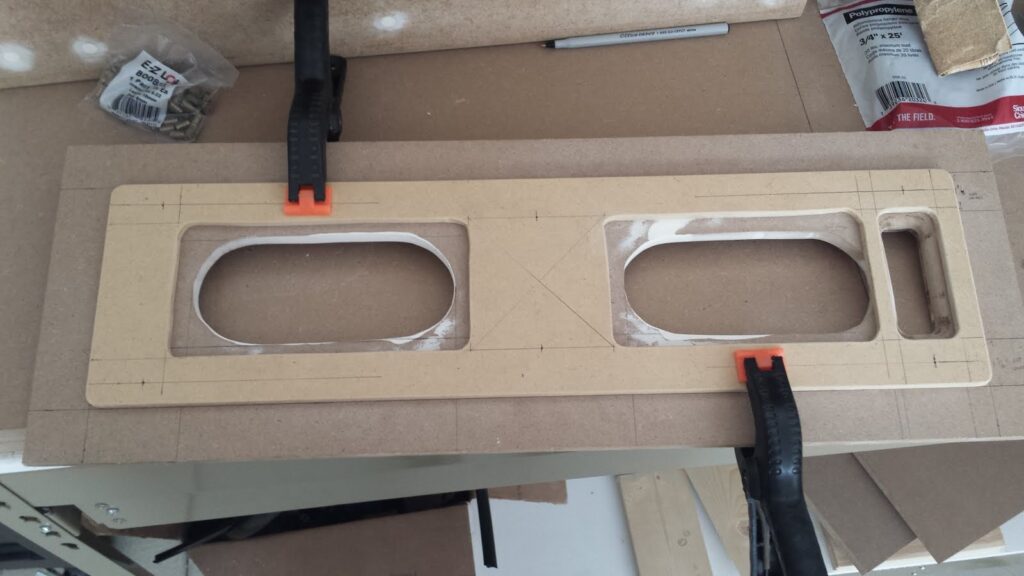 Rectangular section of 1/4-inch MDF clamped to another piece of 1/2-inch MDF.  On both pieces, various holes are cut to allow placement of speakers behind the panel.
