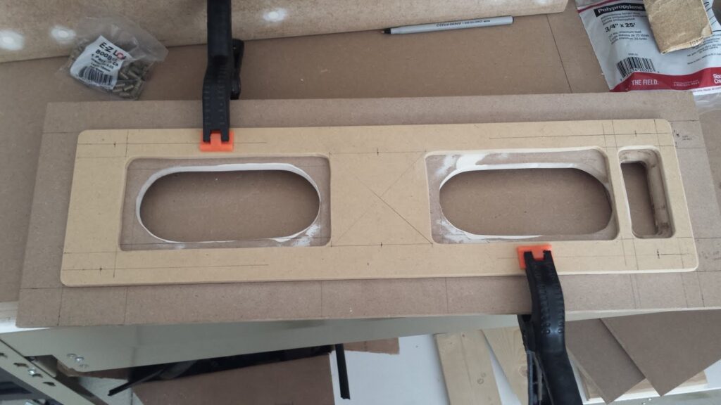 Rectangular section of 1/4-inch MDF clamped to another piece of 1/2-inch MDF. On both pieces, various holes are cut to allow placement of speakers behind the panel.